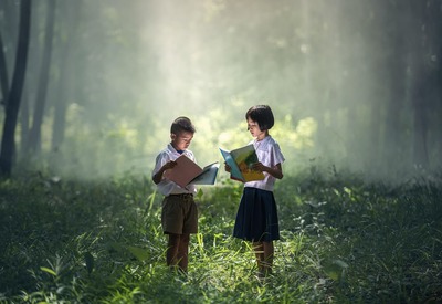 Um casal de crianças lendo seus livros em pé em meio à natureza circundante